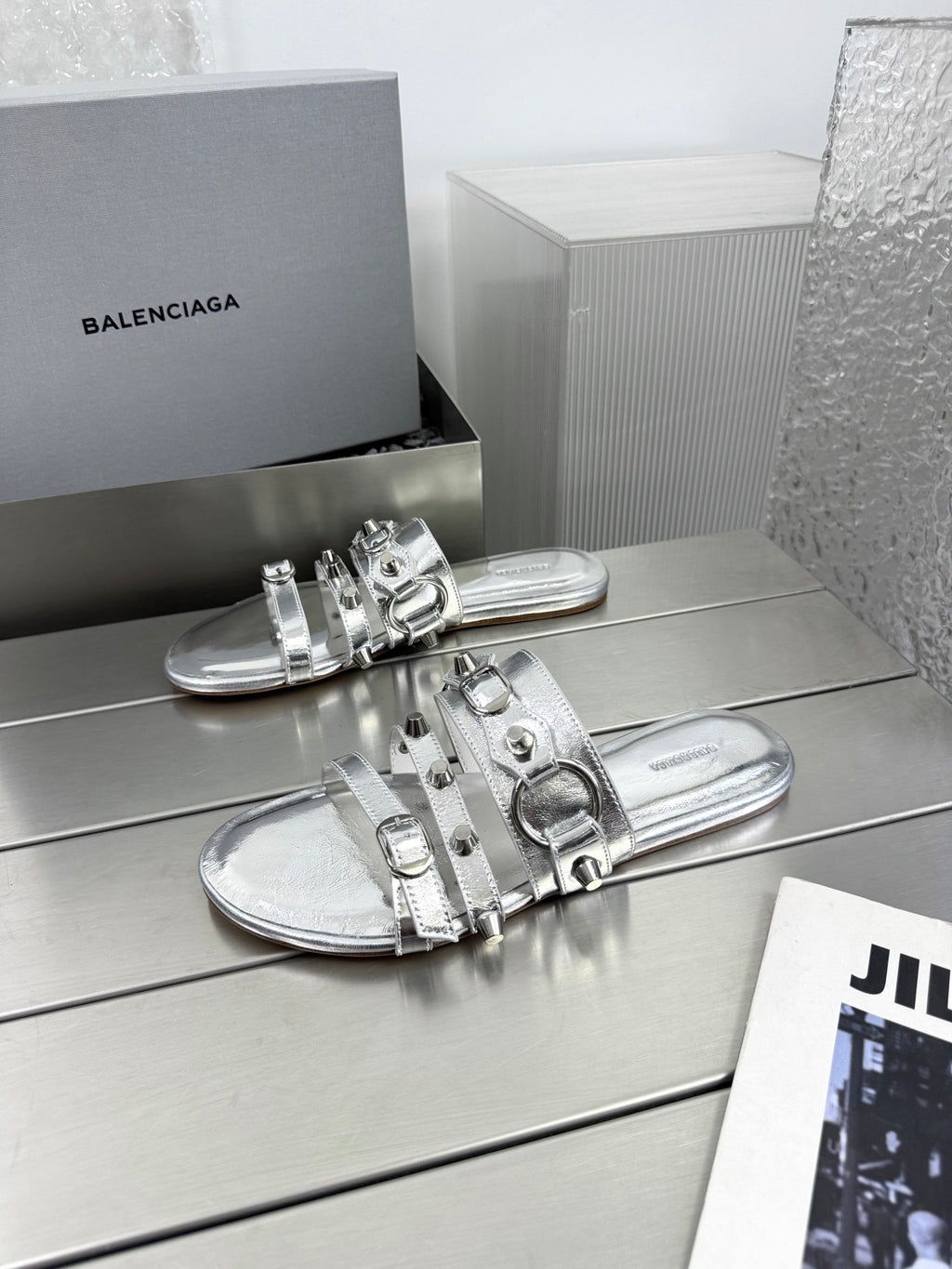 Silver metallic slide sandals with studded straps and buckle details