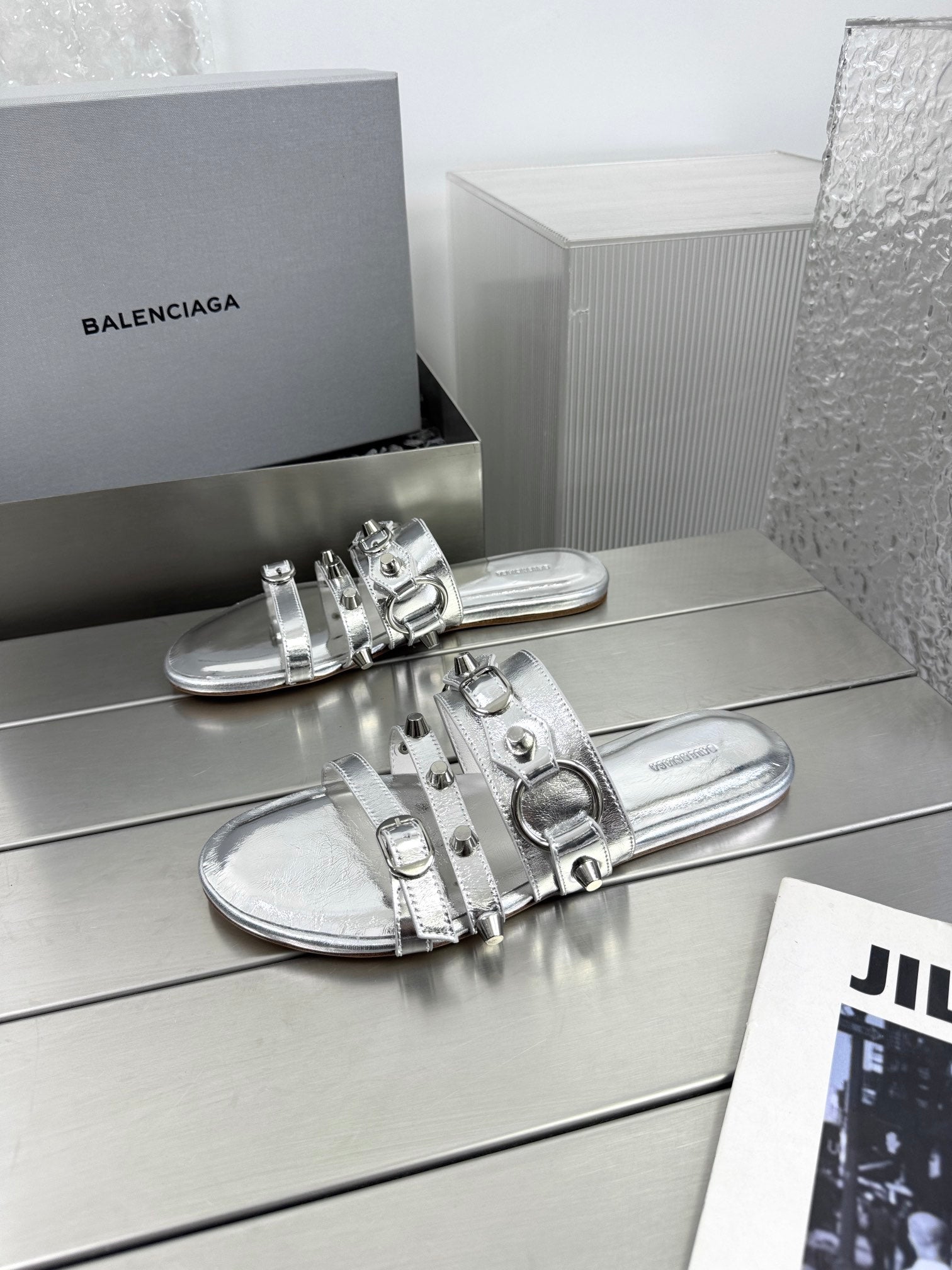 Silver metallic slide sandals with studded straps and buckle details