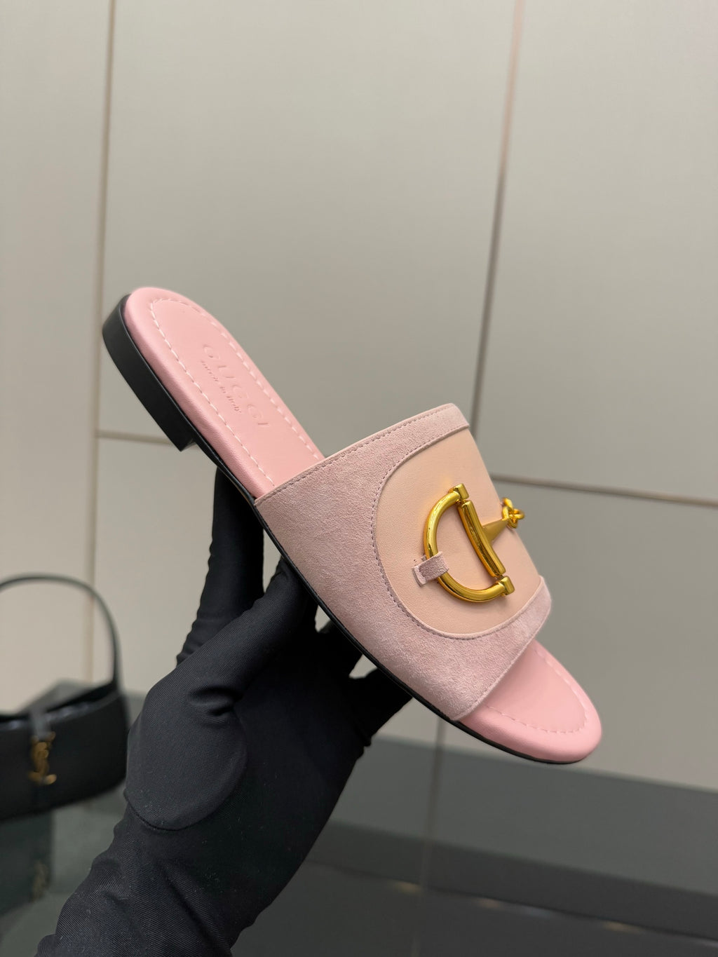 Light pink Gucci slide sandal with gold H-bit strap and wide band, held at an angle