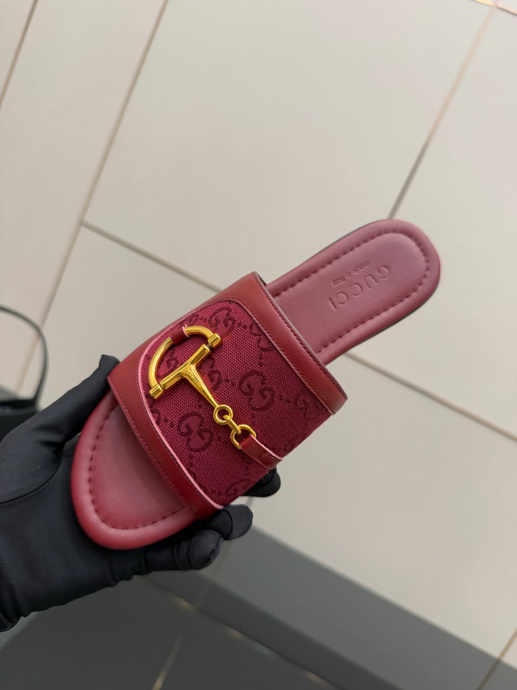 Gucci slide sandal close-up: dark red embossed strap with gold horsebit, hand-held