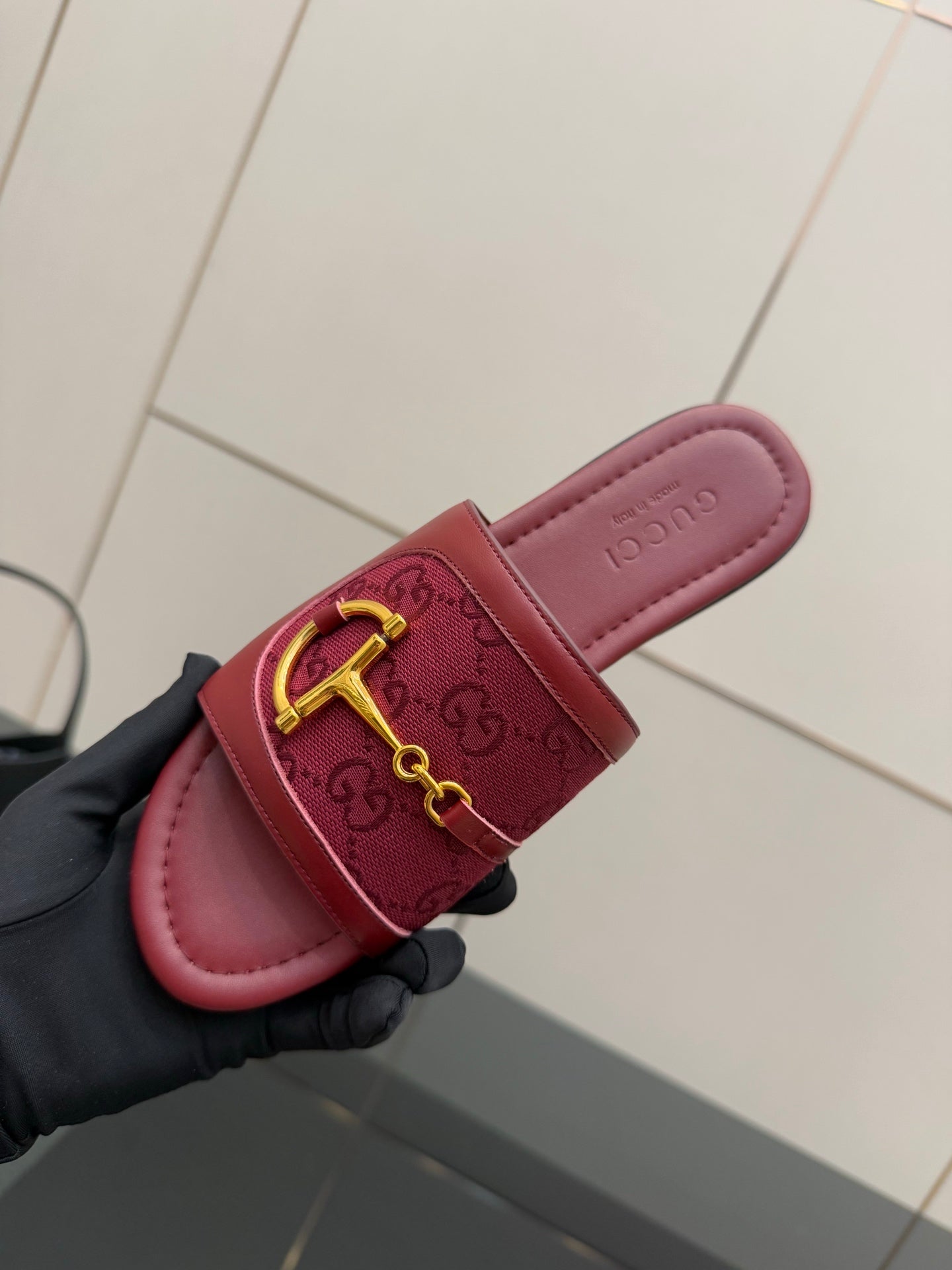 Gucci slide sandal close-up: dark red embossed strap with gold horsebit, hand-held