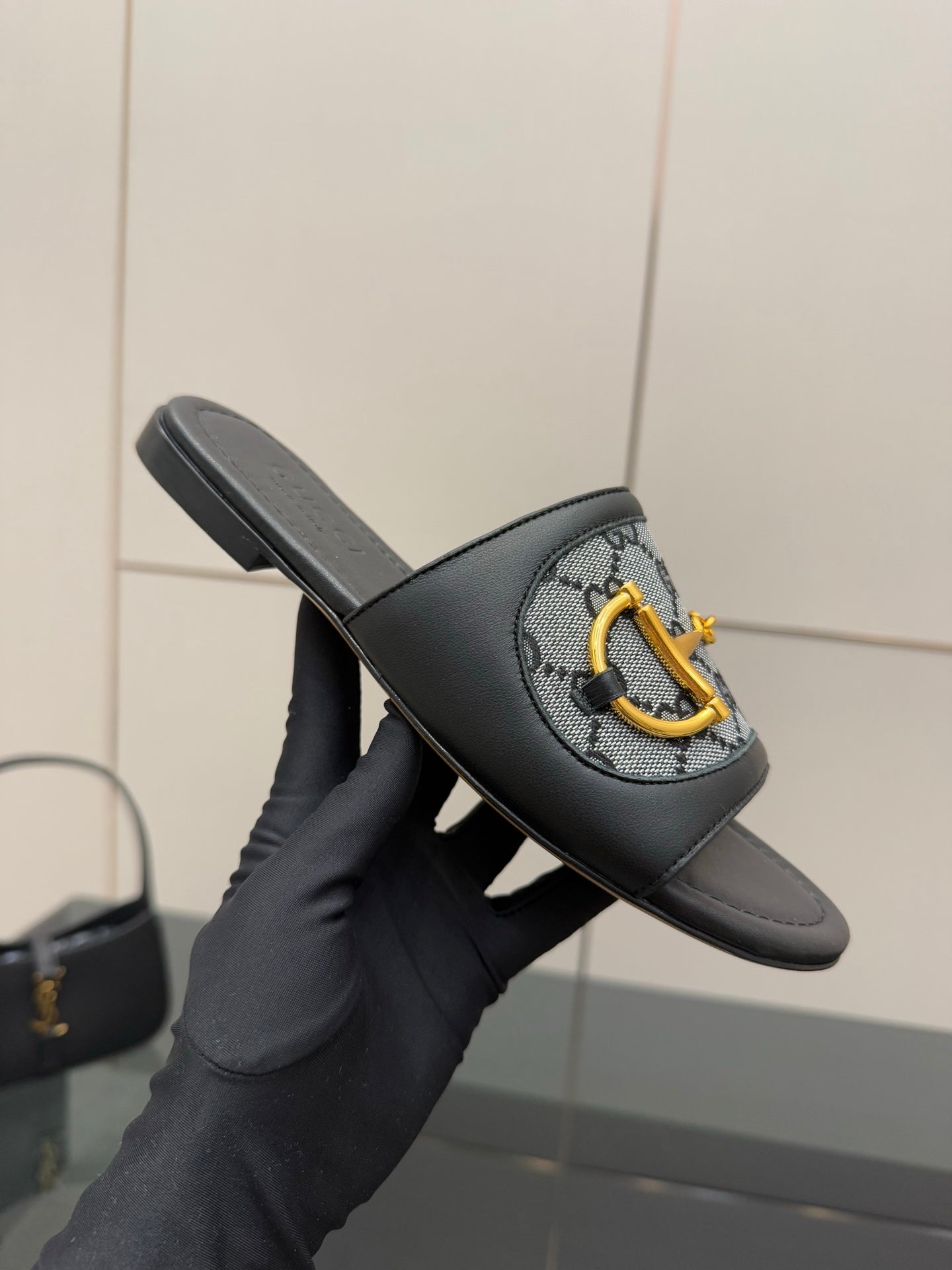 Gucci ladies slide sandal held up, black leather band with gray GG panel and yellow hardware