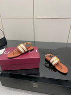 Pair of tan flat thong sandals with white striped strap and gold buckle, angled