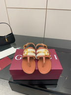 Brown flat thong sandals with white striped straps and gold buckle