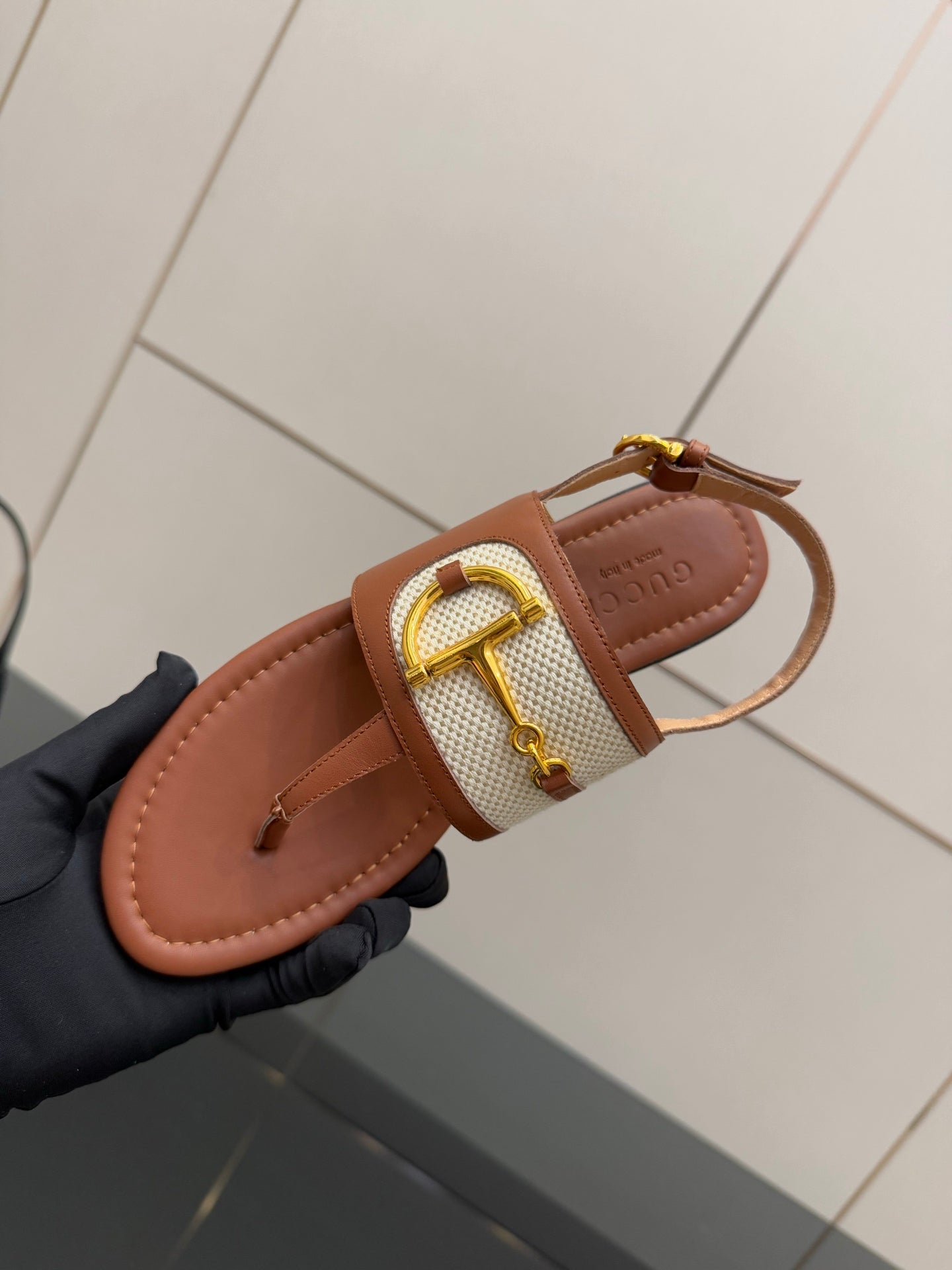 Tan thong sandals with white striped strap and gold buckle, close-up detail