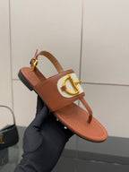 Tan leather thong sandals with white striped strap and gold buckle, held in hand