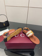Tan flat thong sandals with white striped strap and gold buckle, back view