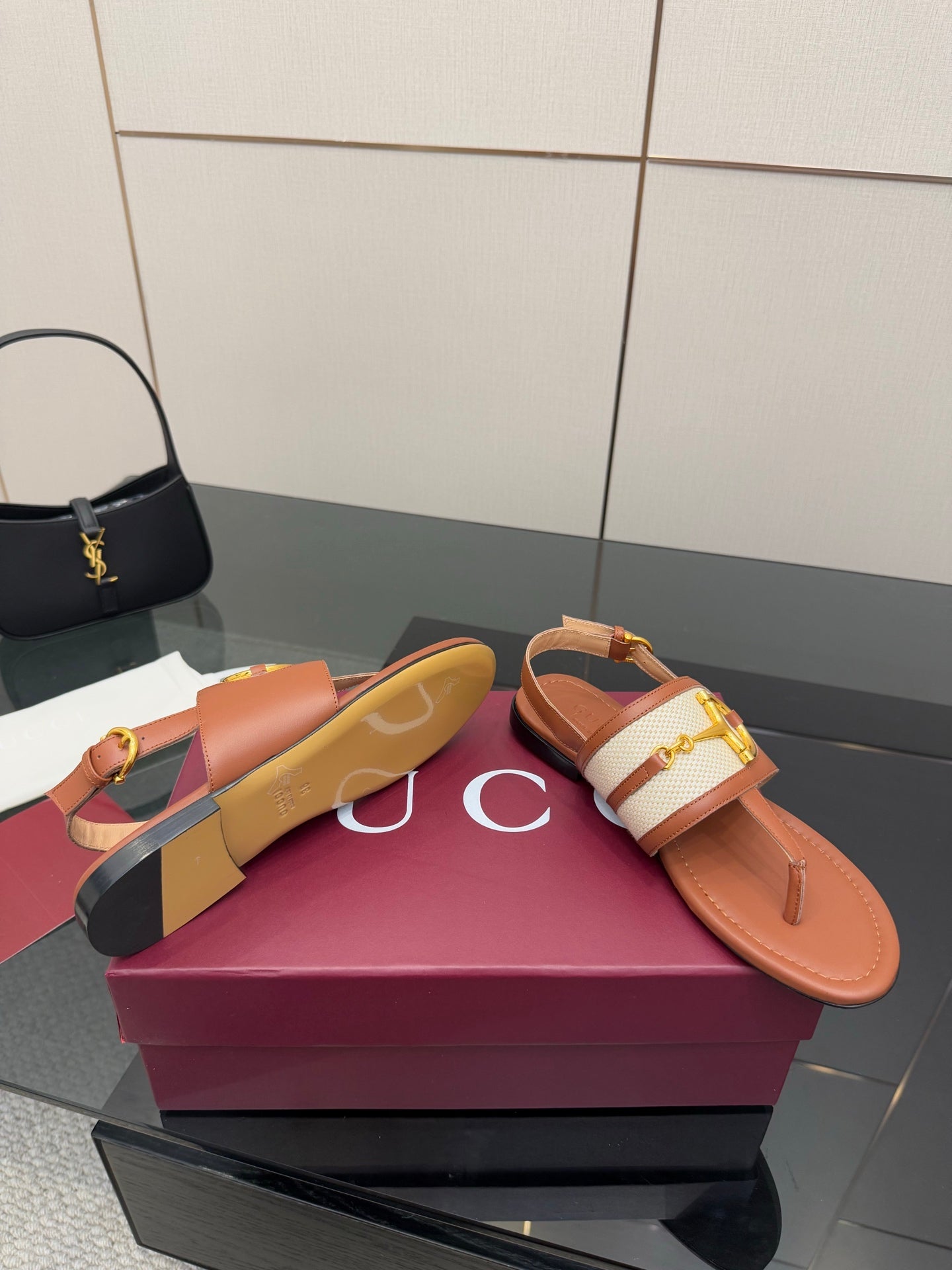 Tan flat thong sandals with white striped strap and gold buckle, back view