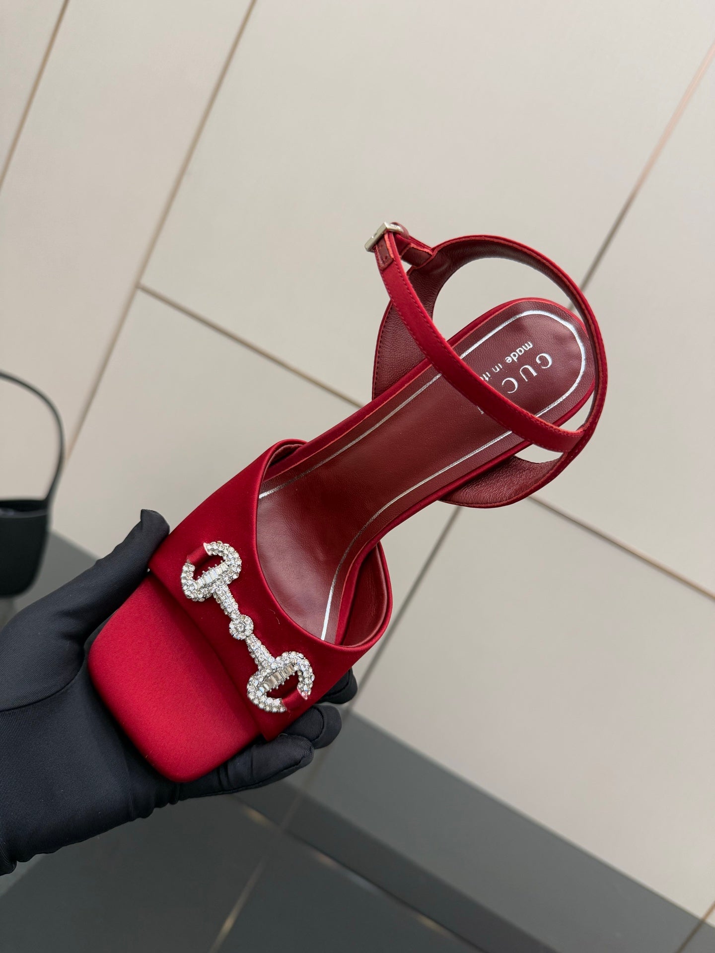 Red Gucci sandals held in hand, showing rhinestone horsebit strap detail