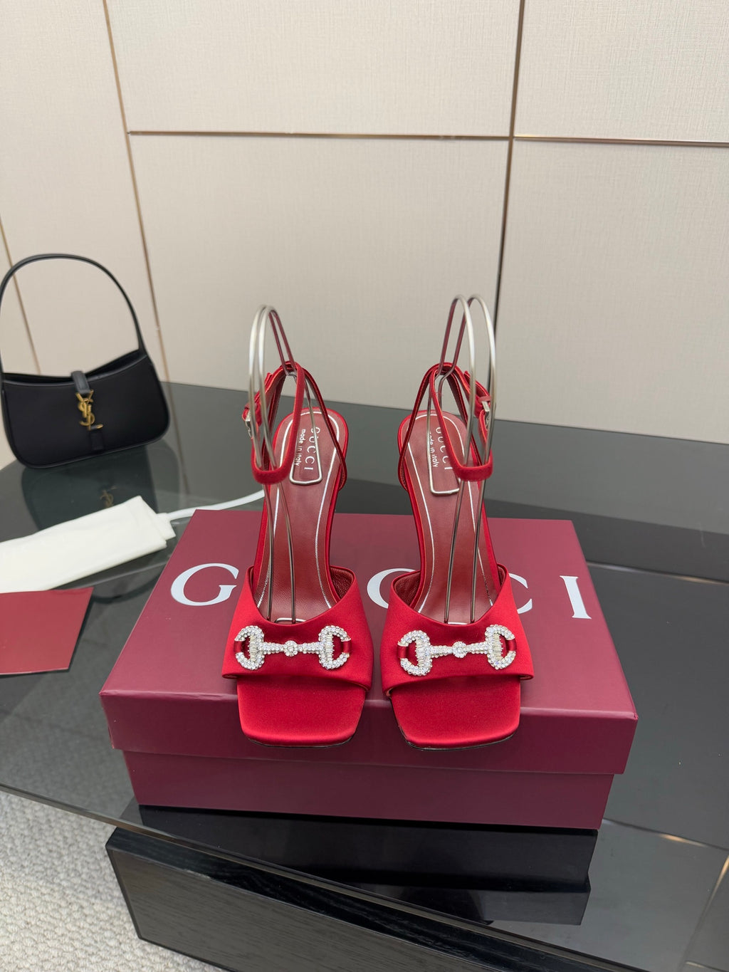Red heeled sandals with decorative silver buckle detail, pair displayed on a box