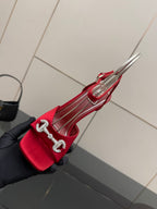 Red heeled sandal with clear straps and silver buckle detail, close-up held in glove