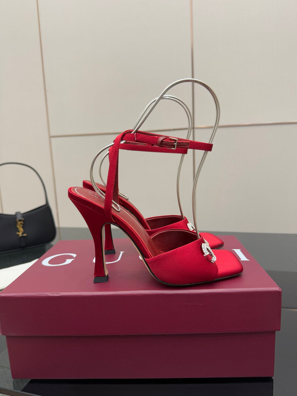 Red heeled sandal with clear ankle straps and silver buckle detail, angled on box