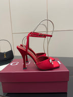 Red heeled sandal with clear ankle straps and silver buckle detail, angled on box