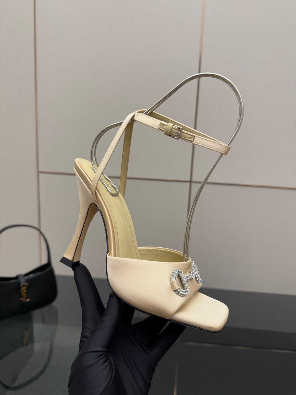 Cream slingback sandal held in glove, rhinestone buckle and stiletto heel