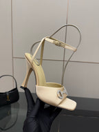 Cream slingback sandal held in glove, rhinestone buckle and stiletto heel