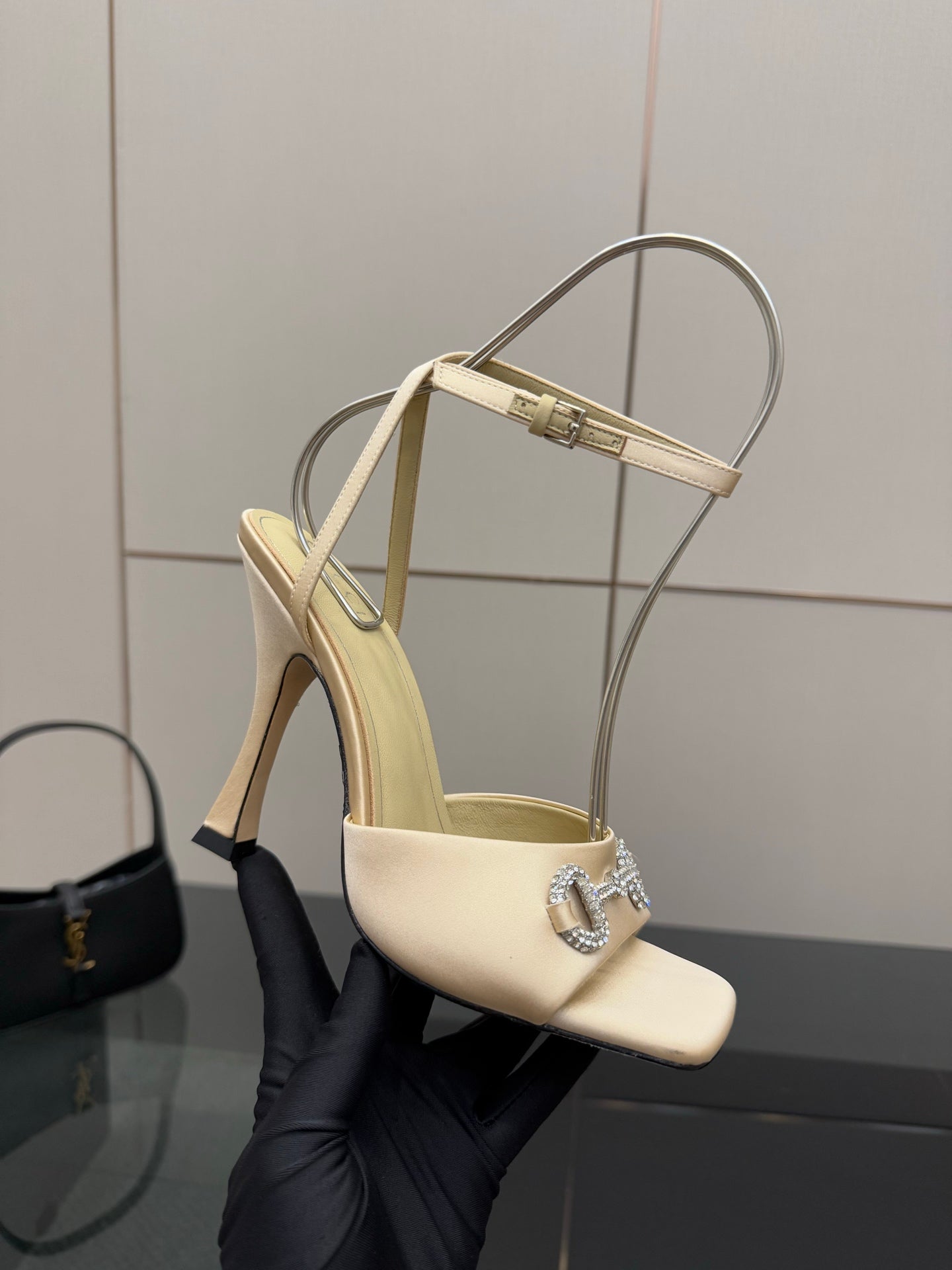 Cream slingback sandal held in glove, rhinestone buckle and stiletto heel
