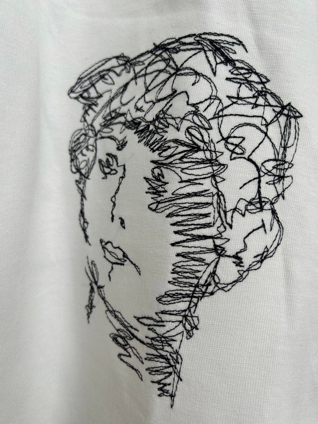 Off-white T-shirt close-up of black line-drawing face graphic