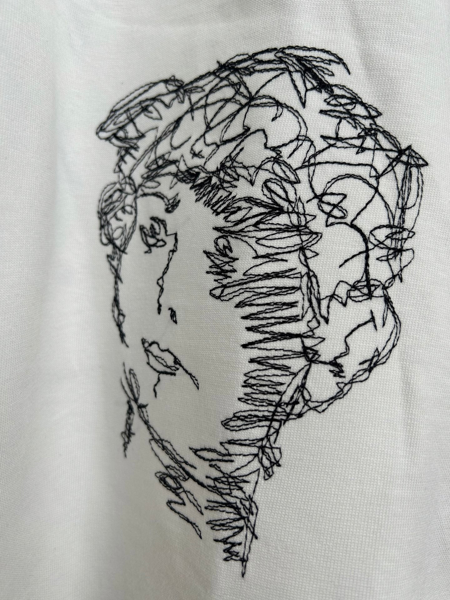 Off-white T-shirt close-up of black line-drawing face graphic
