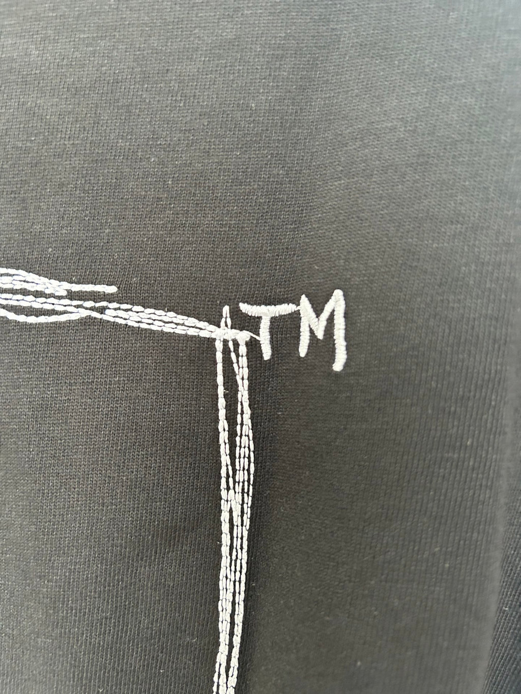Black T-shirt back detail with white embroidered-style “TM” text