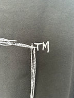 Black T-shirt back detail with white embroidered-style “TM” text