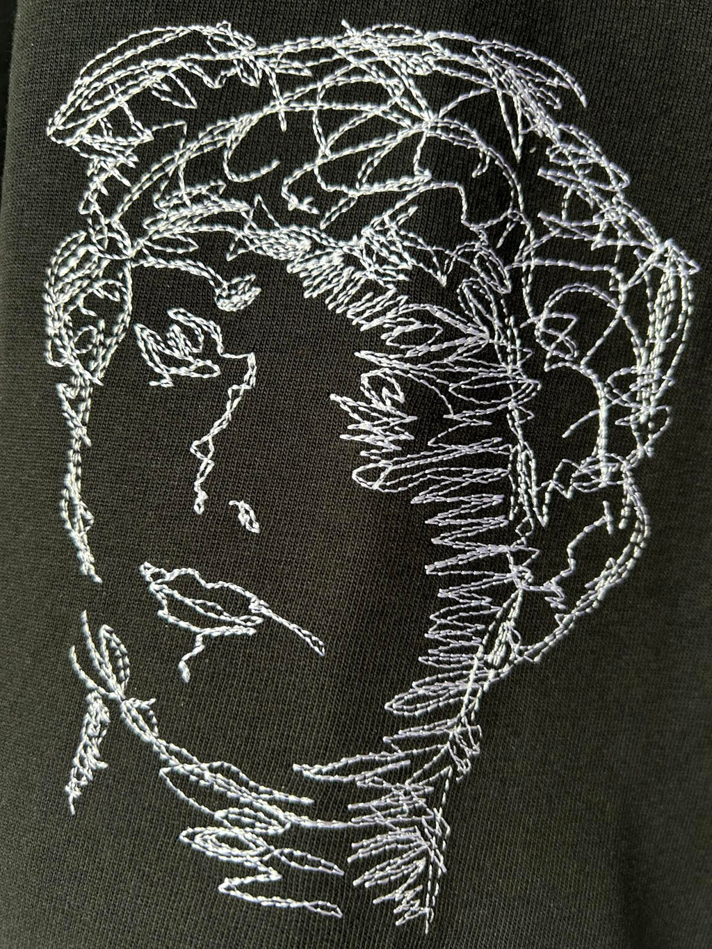 Black T-shirt with circular embroidered-style face sketch graphic in white