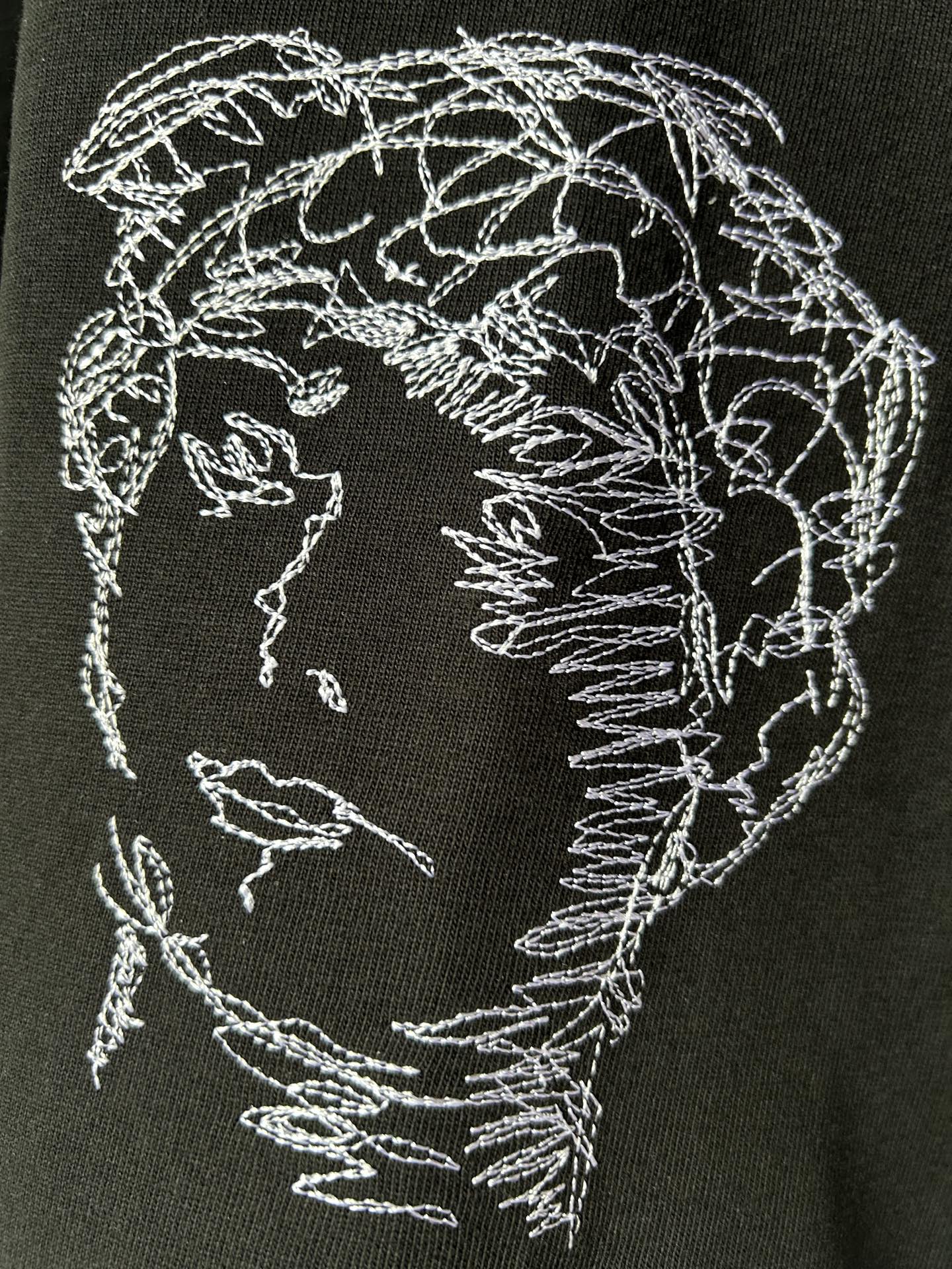 Black T-shirt with circular embroidered-style face sketch graphic in white