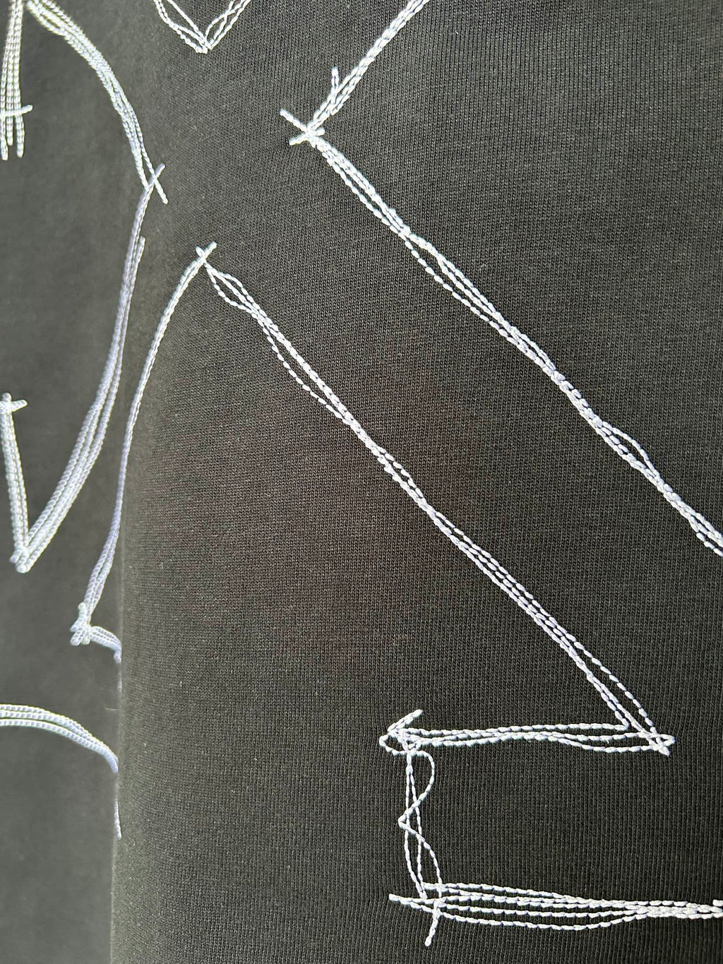 Black T-shirt fabric close-up with white stitched arrow graphic lines