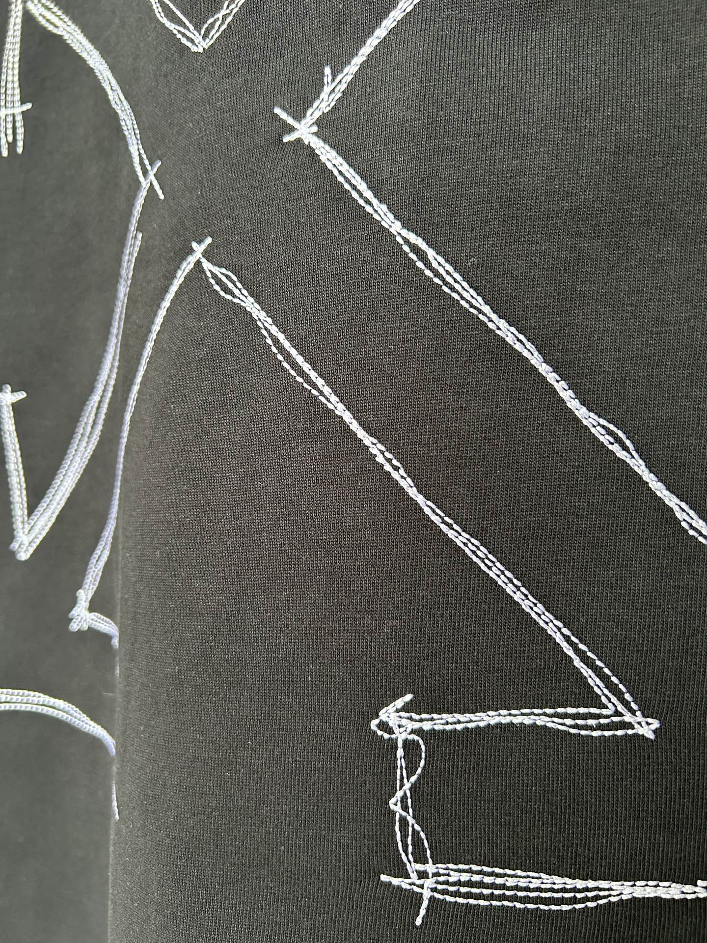Black T-shirt fabric close-up with white stitched arrow graphic lines