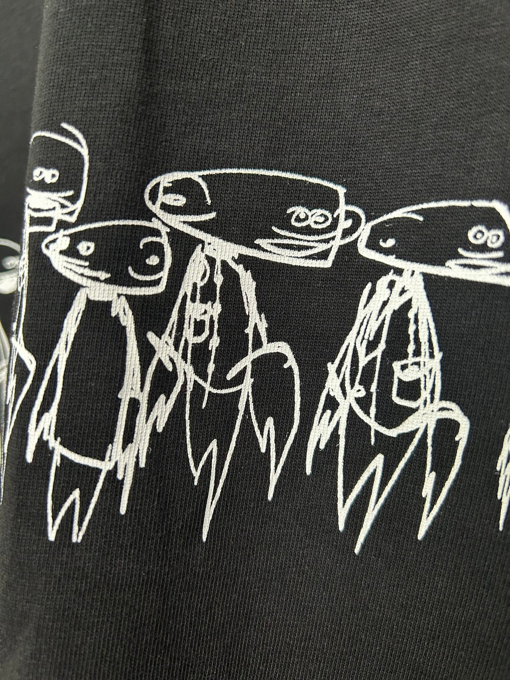 Black T-shirt detail with white outlined character heads and dripping line art