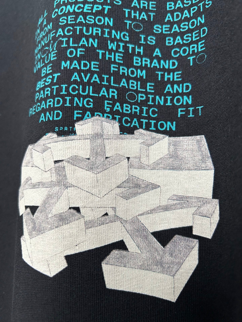 Close-up of dark T-shirt chest graphic with teal text and white abstract print