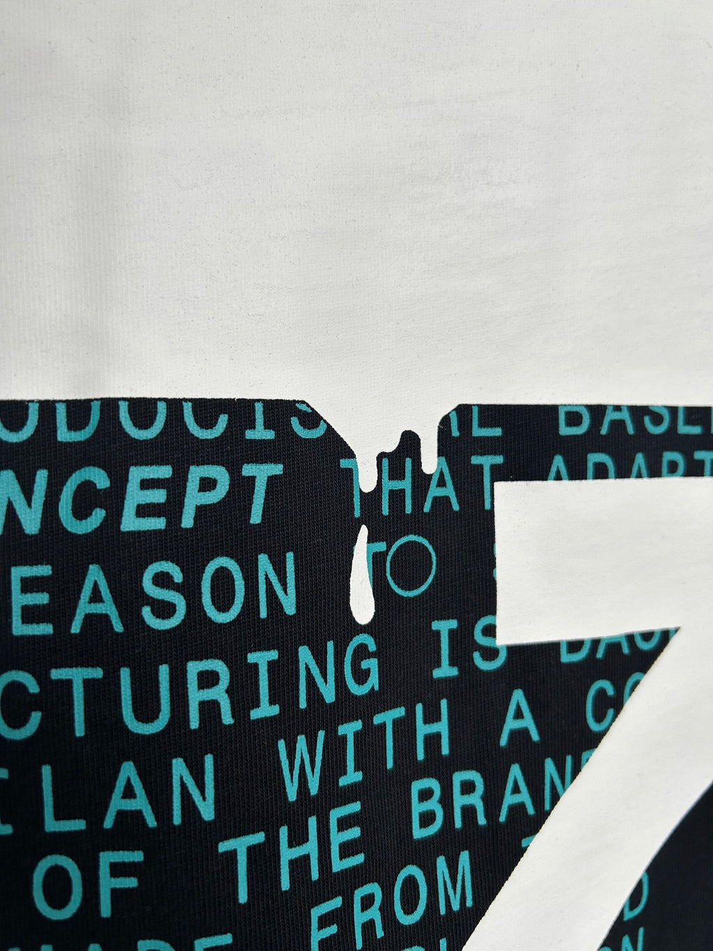 Close-up of dark T-shirt fabric with teal printed text and white graphic overlay