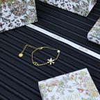 Gold-tone charm bracelet with floral pendant and pearl beads on a printed card.