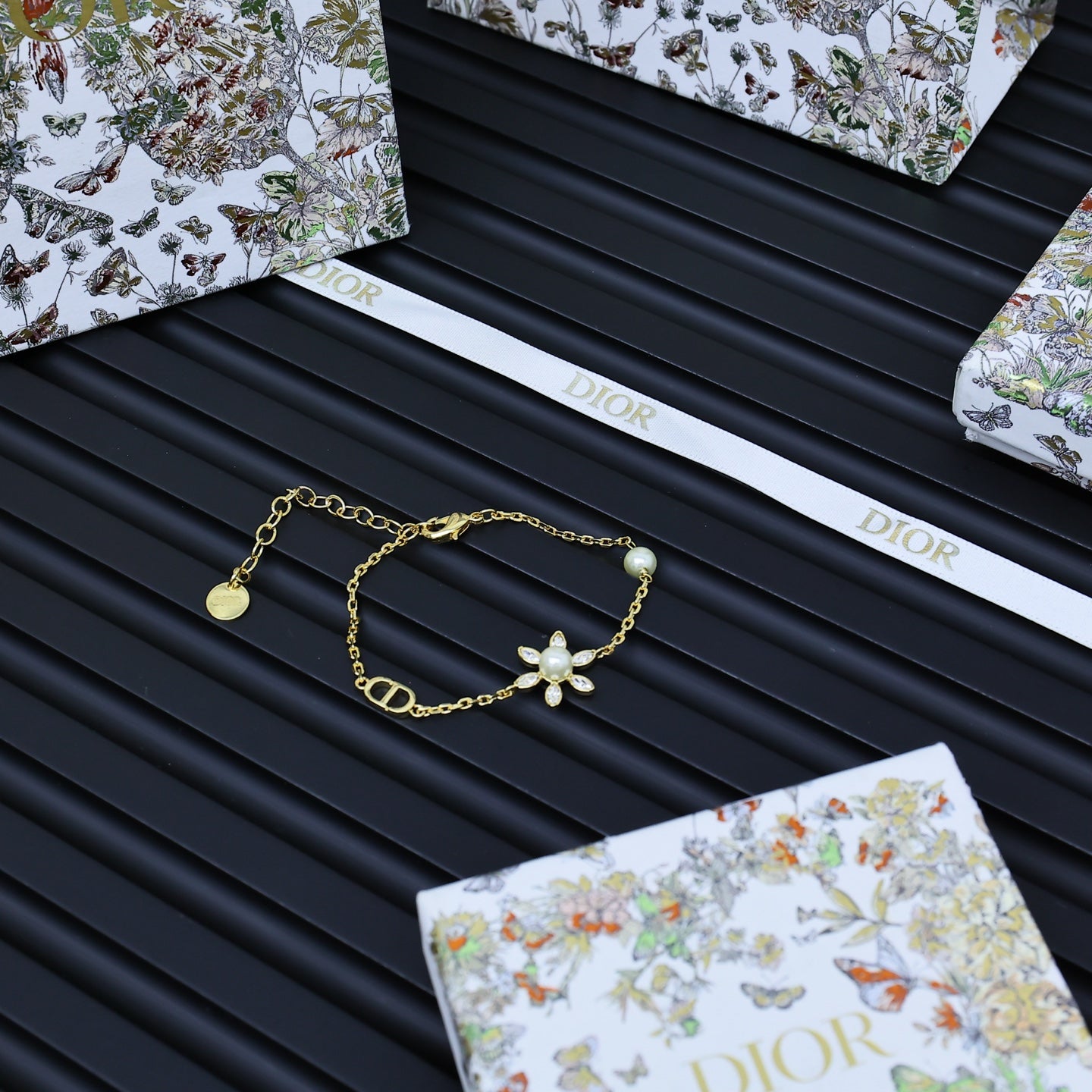 Gold-tone charm bracelet with floral pendant and pearl beads on a printed card.