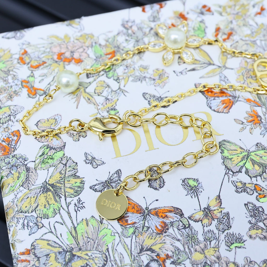 Gold-tone charm bracelet with floral and pearl accents, featuring D-style link detail.