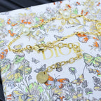 Gold-tone charm bracelet with floral and pearl accents, featuring D-style link detail.