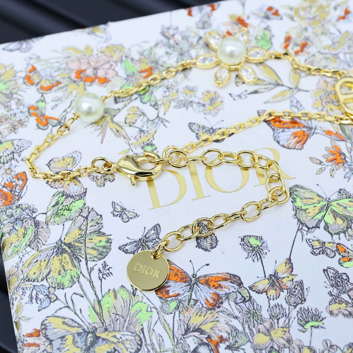 Gold-tone charm bracelet with floral and pearl accents, featuring D-style link detail.