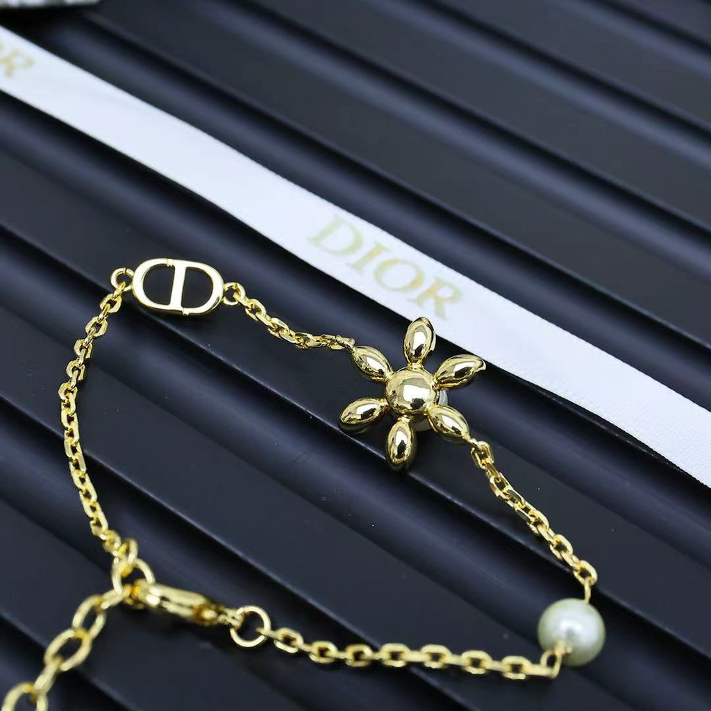 Gold-tone charm necklace with D-style clasp, flower pendant, and pearl bead.
