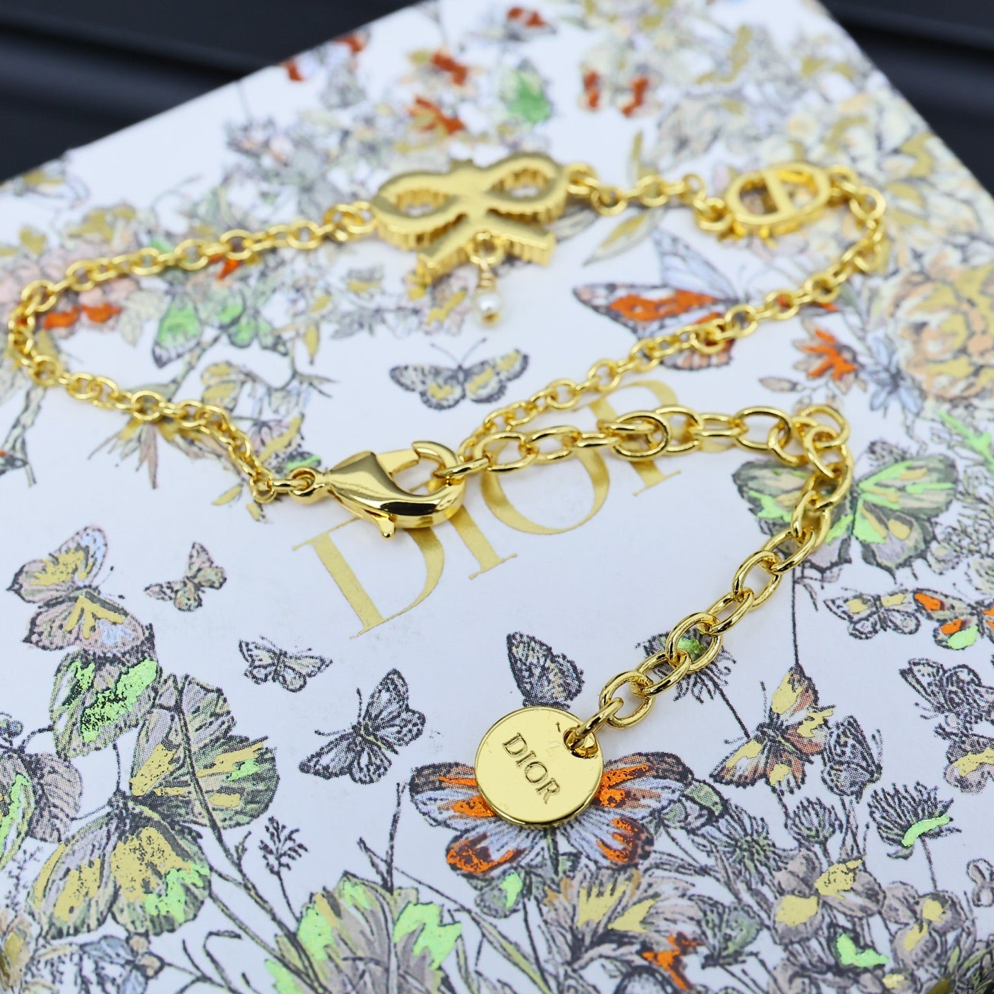 Gold-tone chain bracelet with bow charm and round logo pendant