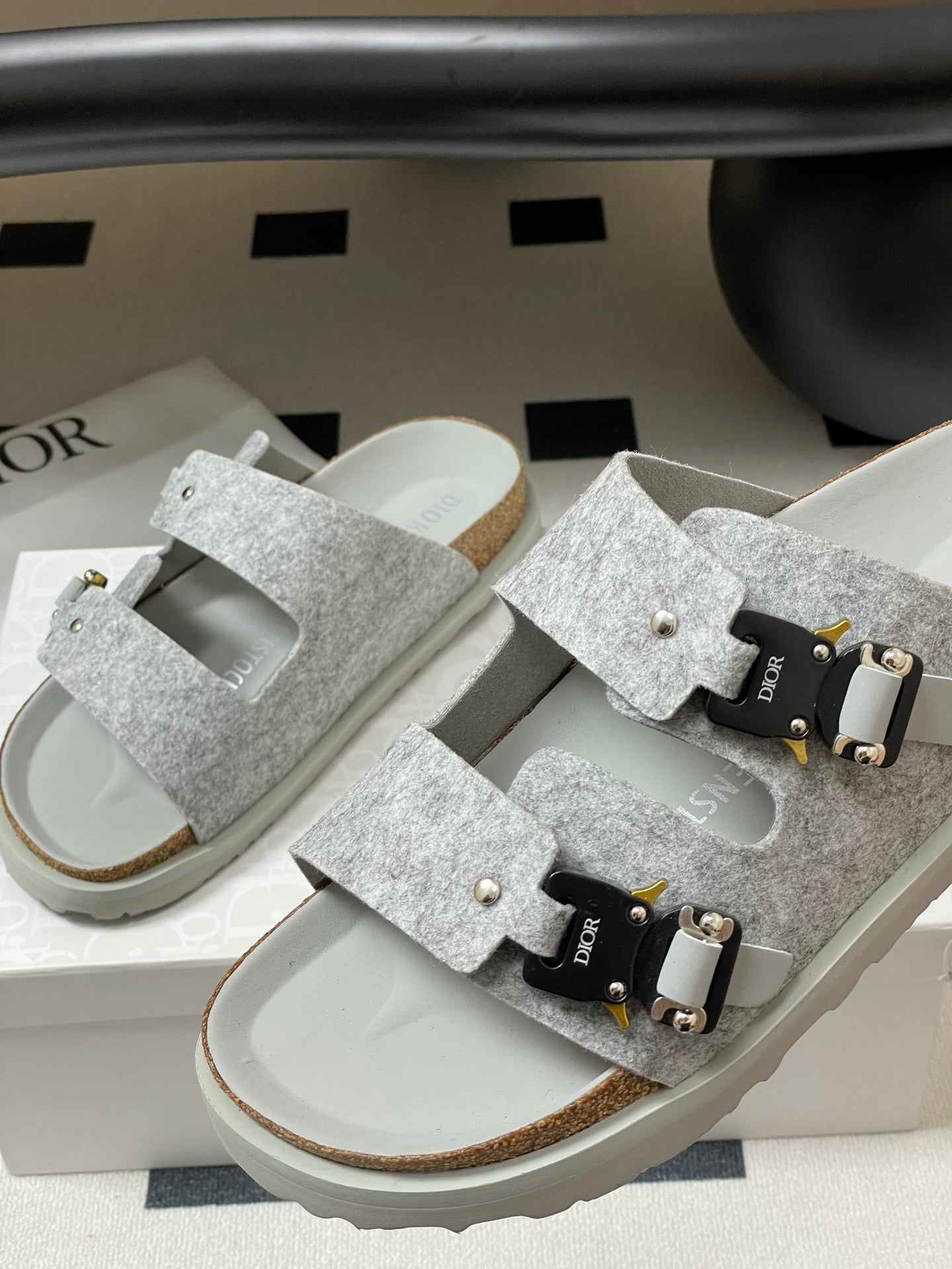 Grey Dior sandals pair with open-toe design, wide straps, and gold buckle hardware