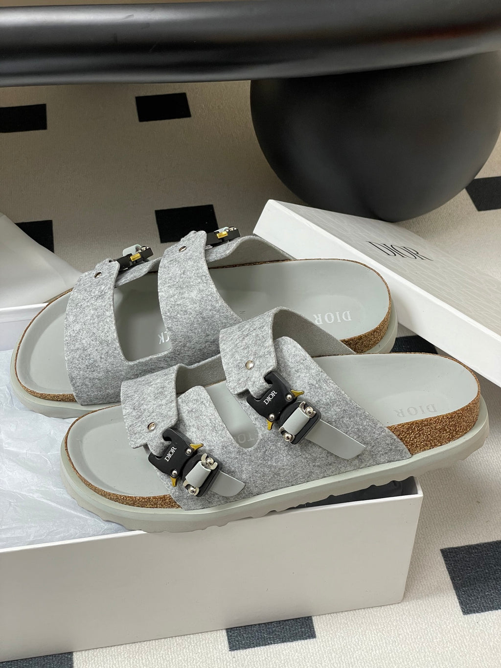 Grey Dior sandals on white box, two wide straps with gold-and-black buckles