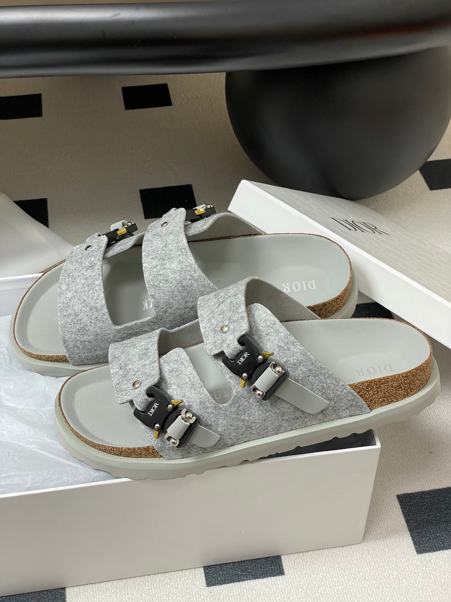 Grey Dior sandals on white box, two wide straps with gold-and-black buckles