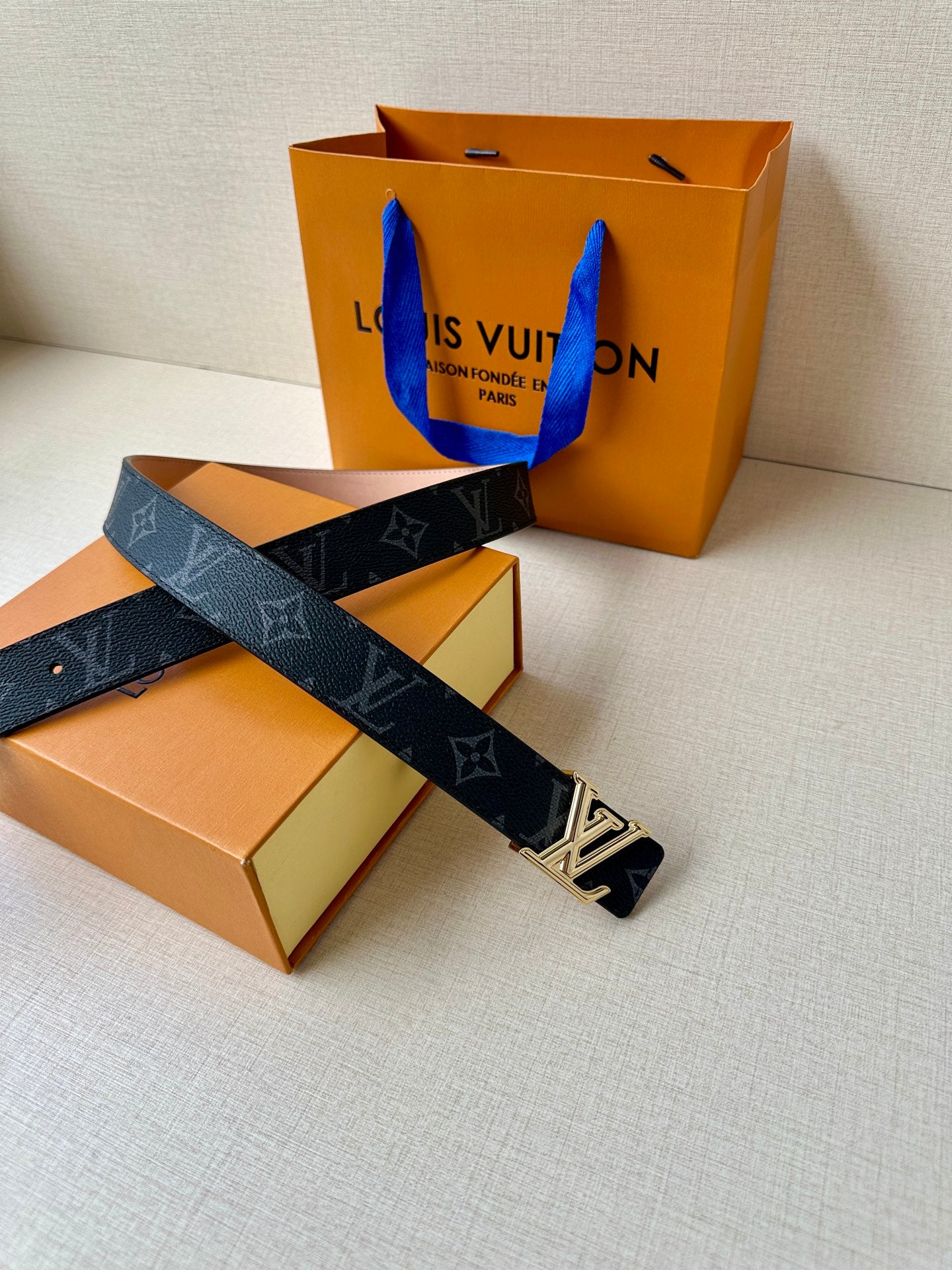 Louis Vuitton monogram belt laid across boxes, dark strap and silver buckle