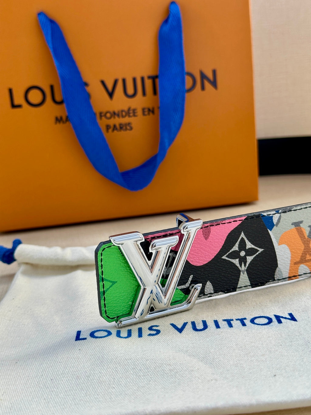 Louis Vuitton belt with gold LV buckle and colorful printed band over dark backing