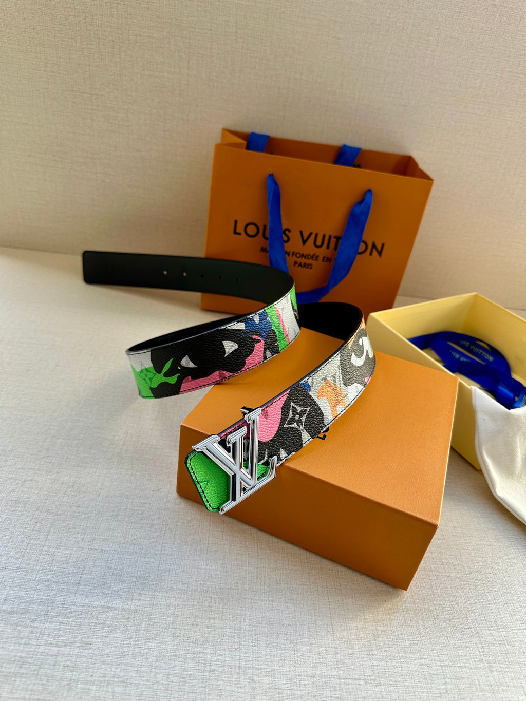 Louis Vuitton belt resting flat, featuring multicolor print strap and gold LV buckle