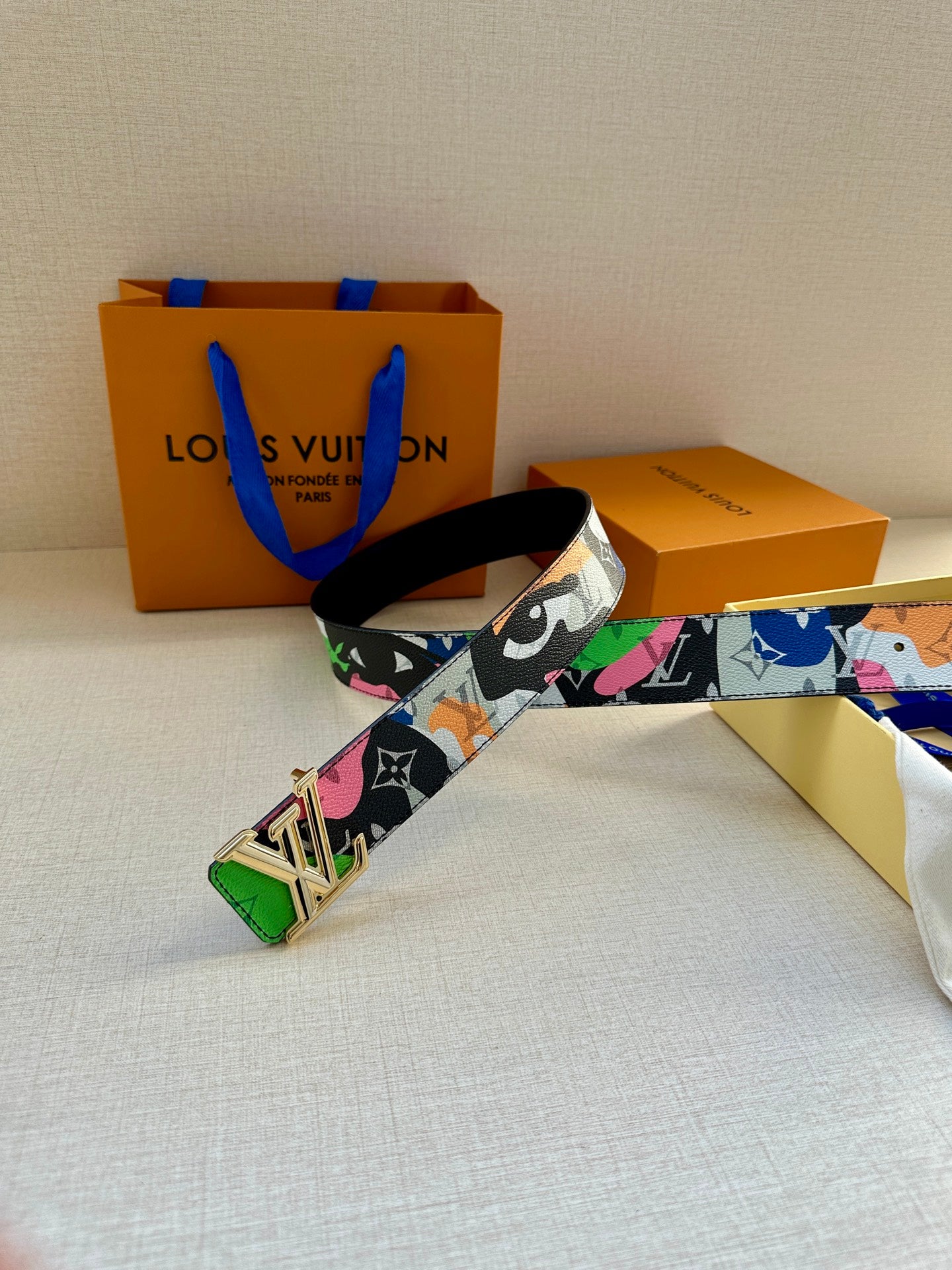 Louis Vuitton belt with graphic strap and gold LV buckle lying across the surface