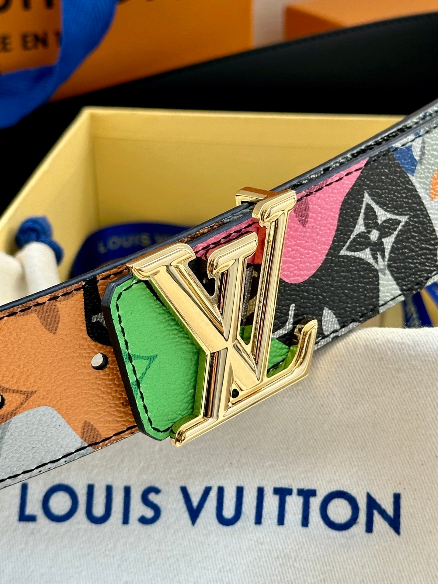 Louis Vuitton belt close-up: gold LV buckle with green edge accent on graphic strap