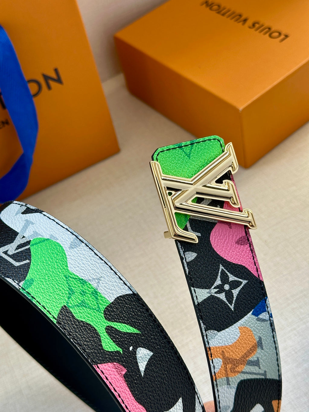 Louis Vuitton belt buckle close-up on multicolor printed strap with green leather tab