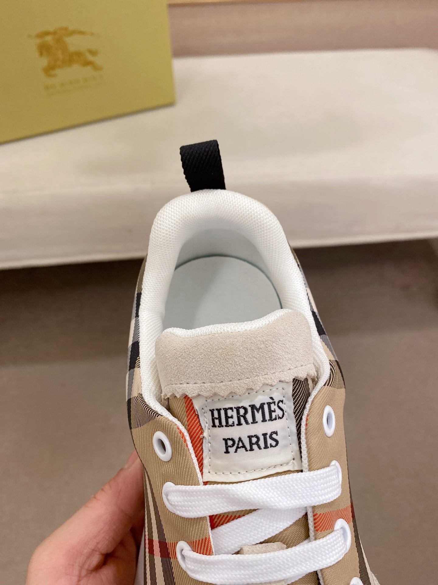 Close-up of plaid canvas sneaker tongue with 'HERMES PARIS' label and white laces.