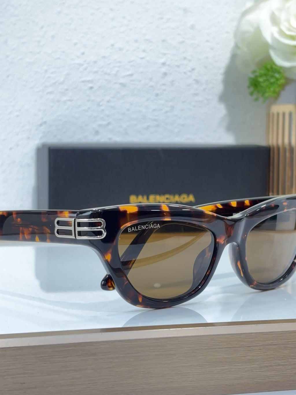 Balenciaga sunglasses, tortoise frame close-up, gold B emblem, amber-tinted lenses