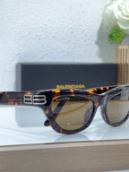 Balenciaga sunglasses, tortoise frame close-up, gold B emblem, amber-tinted lenses